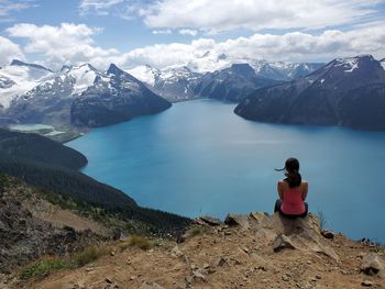 Rear view of man sitting on mountain against sky