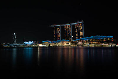 Illuminated city by river against sky at night