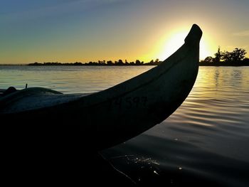 Silhouette boat moored on sea against sky during sunset