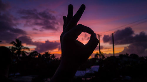 Close-up of silhouette hand showing ok sign against sky during sunset