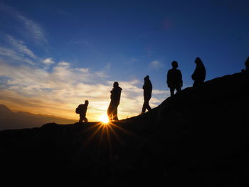 Silhouette people standing on land against sky during sunset