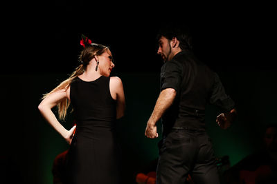 Rear view of people dancing against black background