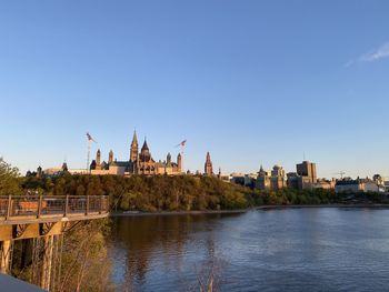 View of buildings by river against clear blue sky