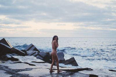 Portrait of naked woman standing on rock at beach