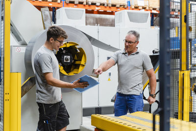 Mature male worker explaining colleague while standing by machinery in industry