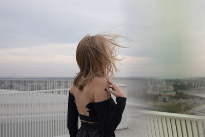 Woman standing by railing against sea against sky