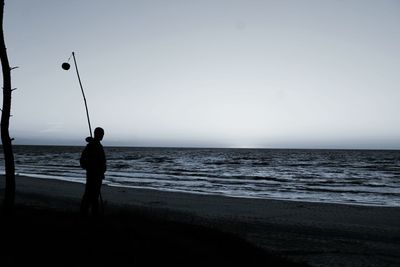 Rear view of man fishing on beach against clear sky