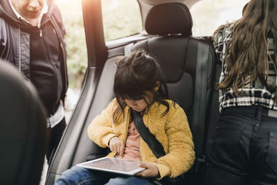 Smiling girl using digital tablet while sitting in car