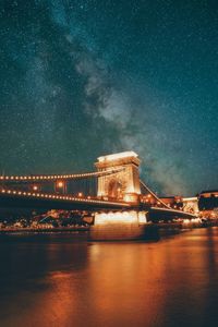 Illuminated bridge over river against sky at night