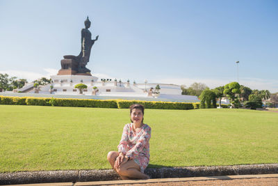 Woman sitting on footpath against sky