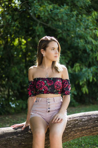 Thoughtful teenage girl looking away while sitting against trees in park