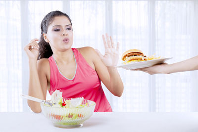 Woman with salad bowl refusing burger at home