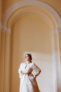 Young woman in dress standing against wall