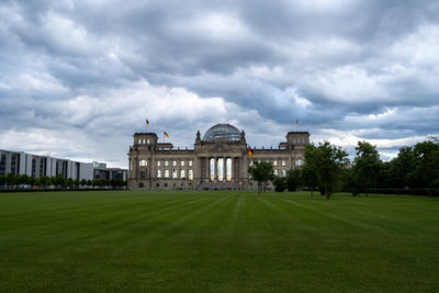 Lawn in front of building against cloudy sky