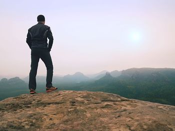 Nature hiker on sharp cliff. terrible rain with thick fog. man alone thinking with hands in pocket.