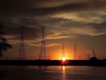 Silhouette electricity pylons on landscape against sky during sunset