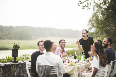 Cheerful male and female friends enjoying dinner party in backyard during weekend