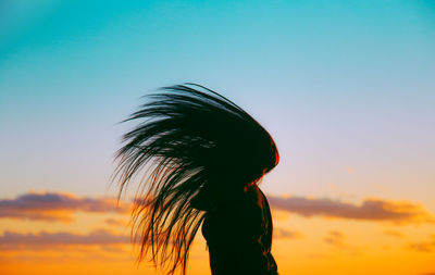 Silhouette woman tossing hair against sky during sunset