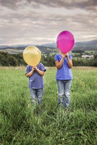 Rear view of people with balloons standing on field against sky