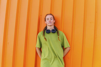 Young woman with hands behind back standing in front of orange wall