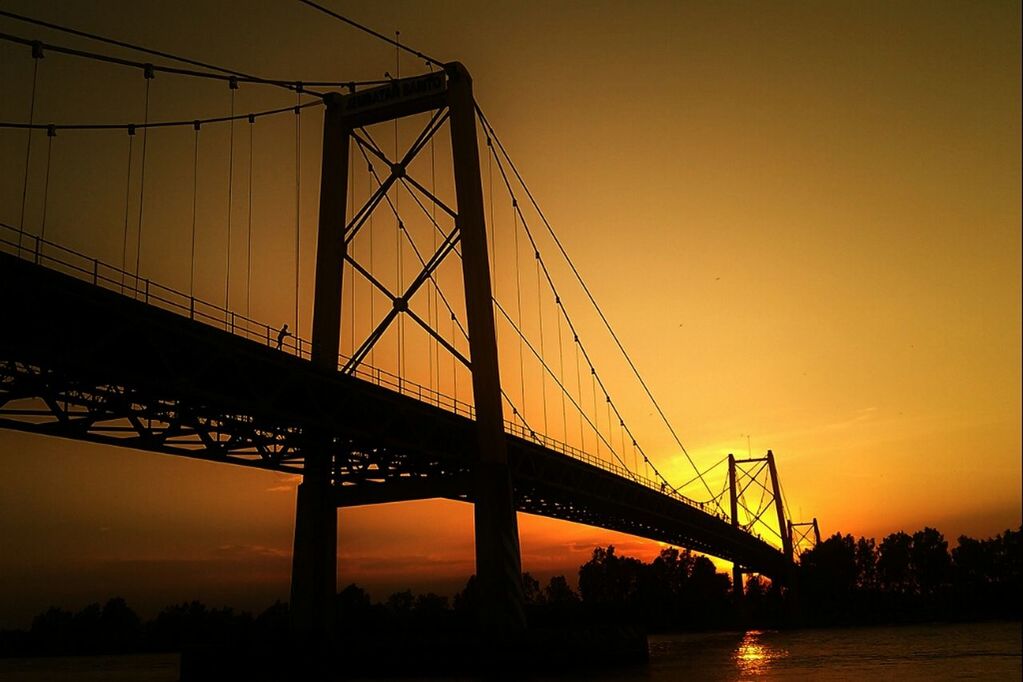 sunset, connection, bridge - man made structure, silhouette, engineering, suspension bridge, built structure, orange color, sun, sky, architecture, bridge, transportation, low angle view, water, river, cable-stayed bridge, outdoors, travel destinations, nature