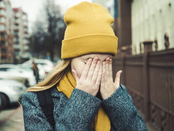 Close-up of woman with hands covering face while standing in city during winter