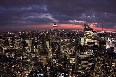 Illuminated buildings in city against cloudy sky