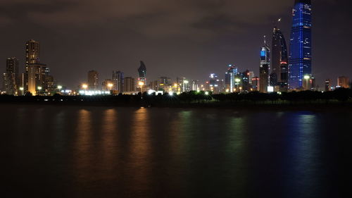 Illuminated buildings by river against sky at night