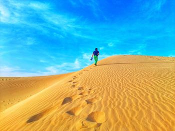 Man walking on sand dune in desert against sky
