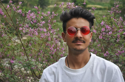 Portrait of young man wearing sunglasses and white tshirt with standing against plants