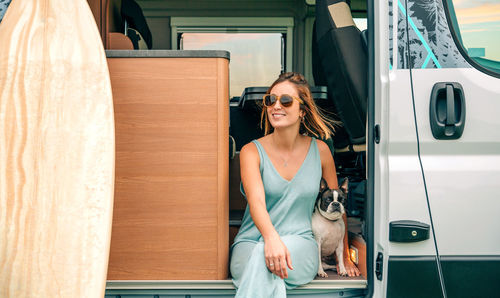 Smiling woman sitting in camper van with dog