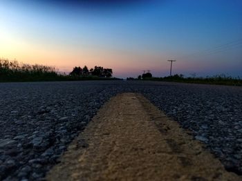 Surface level of empty road against clear sky during sunset