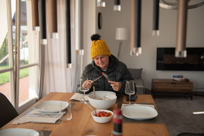 A woman sits at the dining table, dressed warmly, and eats