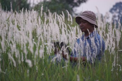 Man using digital tablet while sitting amidst grass on land