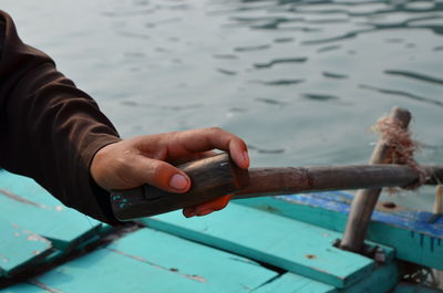 Cropped hand holding oar on boat in sea