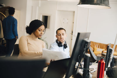 Female computer hacker showing document to male coworker while sitting in office