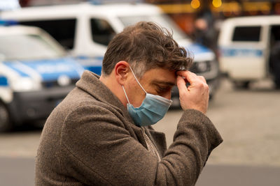 A man wit a medical protective mask with his hands on his head due to receiving bad news or headache