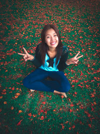 Portrait of smiling woman showing peace sign amidst leaves on field