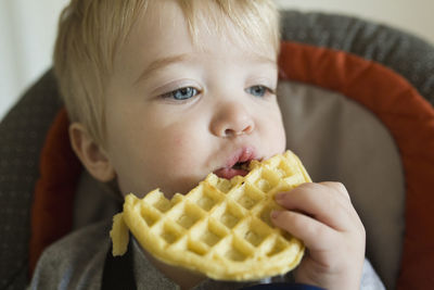 Close-up of cute baby boy eating waffle while sitting on chair at home