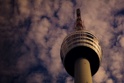 Low angle view of communications tower and building against cloudy sky