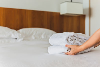 Hands putting stack of fresh white bath towels on the bed sheet