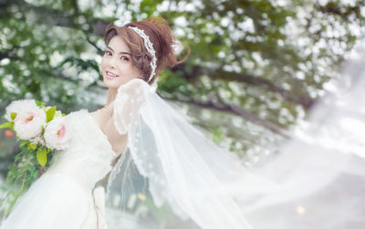 Portrait of smiling bride with bouquet holding veil
