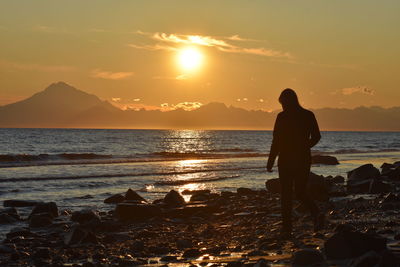 Silhouette man looking at sea against sky during sunset