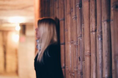 Side view of woman leaning on bamboo wall