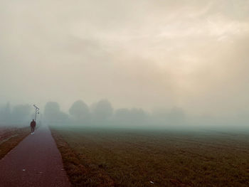 Road amidst field against sky during foggy weather