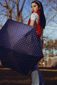 Woman with umbrella standing against bare trees