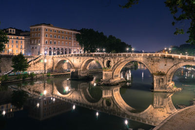 Bridge over river in city against sky at night