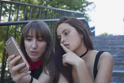 Two young women sitting on a staircase with a smart phone