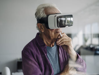 Thoughtful businessman with hand on chi using virtual reality headset while standing in office