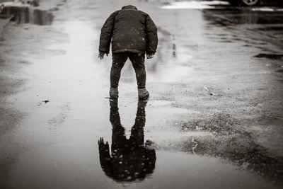 Rear view of boy standing on wet footpath during winter